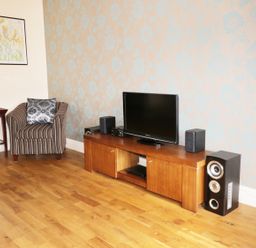 A room with a striped armchair a wooden side table with a lamp a wooden TV stand with a flat screen TV and speakers at William Court Cottage Irton Hall near Wastwater