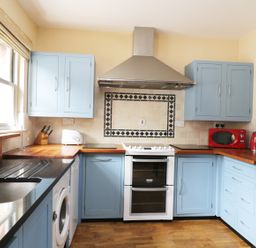 A kitchen with blue cabinets wooden countertops a white stove a red microwave and kettle at William Court Cottage Irton Hall near Wastwater