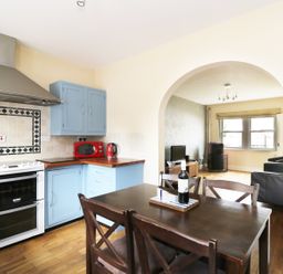 A kitchen with blue cabinets and a wooden table with chairs connected to a living room with a television at William Court Cottage Irton Hall near Wastwater