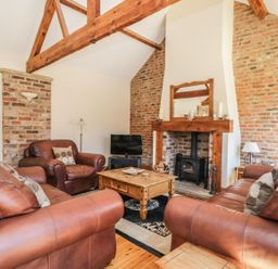 A living room with leather sofas a wooden coffee table a fireplace with wood burner and exposed brick walls at Wheelhouse Cottage in Sowerby outskirts of Thirsk