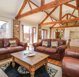 A living room with brown leather sofas a wooden coffee table and exposed wooden beams at Wheelhouse Cottage in Sowerby outskirts of Thirsk