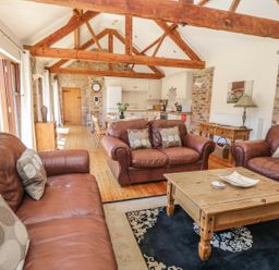 A living area with brown leather sofas and a wooden coffee table opens to a kitchen with wooden beams at Wheelhouse Cottage in Sowerby outskirts of Thirsk