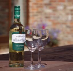 A bottle of Chardonnay and two empty wine glasses on a wooden table outdoors at Wheelhouse Cottage in Sowerby outskirts of Thirsk
