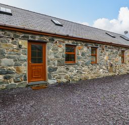 A stone exterior wall of a building with wooden doors and windows and a gravel ground at Cefn-Yr-Efail in Golan near Porthmadog