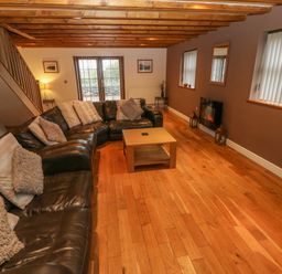 A living room with a brown leather sofa and cushions wooden coffee table wooden floor and ceiling beams at Cefn-Yr-Efail in Golan near Porthmadog