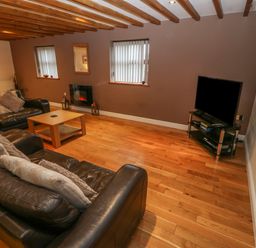A living room with leather sofas a wooden coffee table a TV on a stand and wooden beams on the ceiling at Cefn-Yr-Efail in Golan near Porthmadog