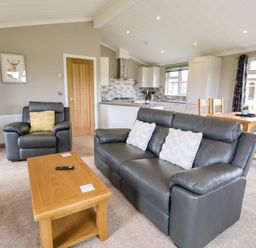 A living room with gray leather sofas and a wooden coffee table next to a kitchen and dining area at Callow Lodge 15 Beaconsfield Farm Holiday Park near Shrewsbury