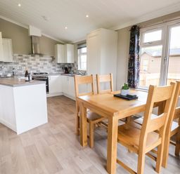 A kitchen and dining area with wooden table and chairs near a window at Callow Lodge 15 Beaconsfield Farm Holiday Park near Shrewsbury