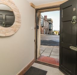 An open black front door with a round wall mirror reflecting a door opposite at Jackson Cottage in Alnmouth
