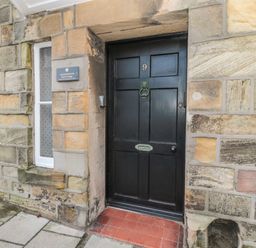 A black front door with the number 9 on a stone wall with a small window to the left at Jackson Cottage in Alnmouth