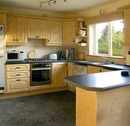 A kitchen with wooden cabinets black countertops a refrigerator oven microwave and a window showing greenery at 19 River Glen in Curracloe County Wexford