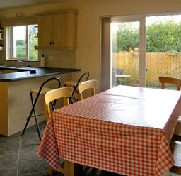A kitchen and dining area with a checkered tablecloth on the table and sliding glass doors opening to a garden at 19 River Glen in Curracloe County Wexford