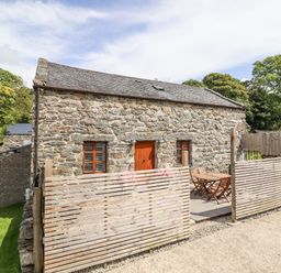 The exterior of a stone cottage with wooden doors and windows a fenced patio with a wooden table and chairs at Isallt Llanfair near Harlech