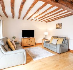 A living room with two gray sofas a wooden TV stand and ceiling beams at Isallt Llanfair near Harlech