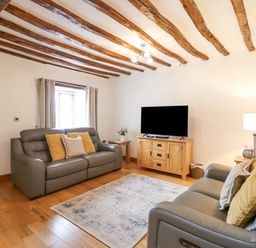 A living room with two leather sofas a tv on a wooden cabinet and exposed wooden ceiling beams at Isallt Llanfair near Harlech