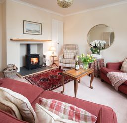 A living room with red sofas a wooden coffee table and a lit fireplace at Barmoor Ridge in Lowick near Holy Island