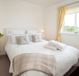 A bedroom with a double bed pillows folded towels bedside tables lamps flowers and yellow curtains at Barmoor Ridge in Lowick near Holy Island