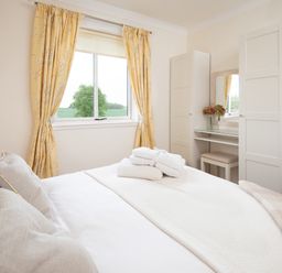 A bedroom with a made bed with towels on it yellow curtains wardrobe and a dressing table at Barmoor Ridge Lowick near Holy Island