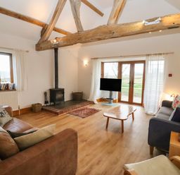 A living room with wooden beams a fireplace two sofas a coffee table a television and large windows at Hill Farm Cottage Kerry's Gate near Abbey Dore