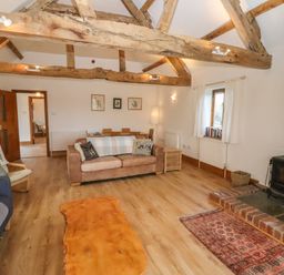 A living room with wooden beams a wood stove a sofa and armchairs at Hill Farm Cottage Kerry's Gate near Abbey Dore