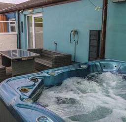 A patio area with a hot tub and outdoor wicker furniture at Barn Cottage in Laugharne