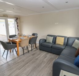A dining area with a wooden table set for six and a dark sectional sofa with cushions at Barn Cottage in Laugharne