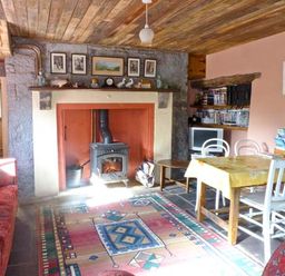 A living room with a wood burning stove a dining table with chairs a red patterned sofa and a colorful rug at Clooncorraun Cottage Ballinrobe County Mayo