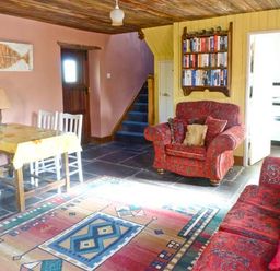 A living room with patterned sofas a wooden table with chairs a carpet on a stone floor and a bookshelf at Clooncorraun Cottage in Ballinrobe County Mayo