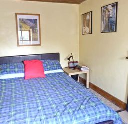 A bedroom with a bed blue checkered bedding and a red pillow two bedside tables with lamps framed pictures on the walls and a fireplace at Clooncorraun Cottage Ballinrobe County Mayo