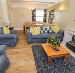 A living room with blue sofas yellow cushions a wooden coffee table with a plant and a dining table at Riverside View in Cark in Cartmel