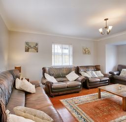 A living room with three brown leather sofas a wooden coffee table an orange patterned rug and wall art at Ingleside Adsett Royal Forest of Dean