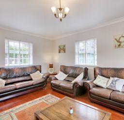 A living room with three brown leather sofas a wooden coffee table with a small plant two windows with white blinds paintings on the walls and a ceiling light at Ingleside in Adsett Royal Forest of Dean