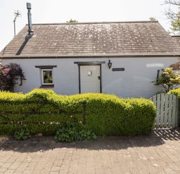 A white house with a grey tiled roof behind a trimmed green hedge and a wooden gate at The Old Stable in Wolfscastle near Haverfordwest