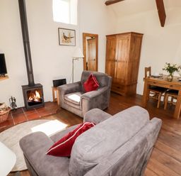 A living room with two armchairs a wood stove and a dining table at The Old Stable in Wolfscastle near Haverfordwest