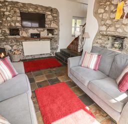 A living room with two gray sofas red rugs a stone wall with a mounted TV and a fireplace at The Coach House in Wolfscastle