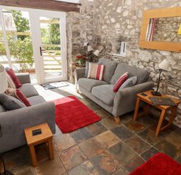 A sitting room with two gray sofas red cushions wooden side tables and stone walls at The Coach House in Wolfscastle