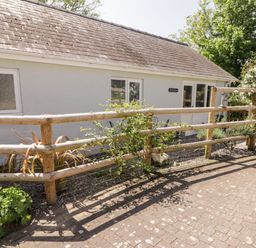 The exterior of a single story building with a wooden fence and plants in front at The Duck House in Wolfscastle