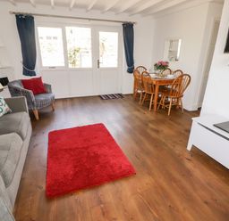 A living room with a sofa and armchair near a red rug and a dining table with chairs at The Duck House in Wolfscastle