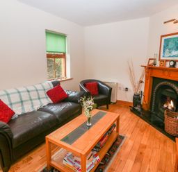 A living room with a leather sofa and armchair a wooden coffee table a fireplace and a window with a green blind at Mary Agnes Cottage in Cahirkeen near Allihies County Cork