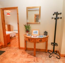 An entryway with wooden stairs a wooden console table with items on it a mirror above and a black coat rack at Mary Agnes Cottage in Cahirkeen near Allihies County Cork