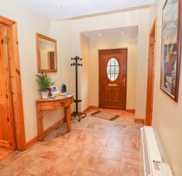 A hallway with a wooden front door a coat rack a wooden table with plants and books a mirror on the wall and a radiator at Mary Agnes Cottage in Cahirkeen near Allihies County Cork