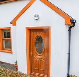 A white house exterior with an orange framed wooden door and window at Mary Agnes Cottage in Cahirkeen near Allihies County Cork
