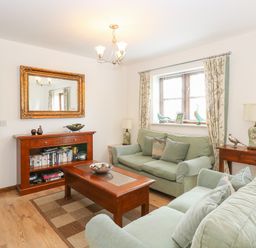 A living room with green sofas wooden coffee table bookshelves and window at The Haybarn in Necton near Swaffham