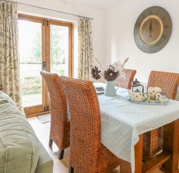 A dining area with wicker chairs a table with a blue cloth and teapot set next to a window at The Haybarn in Necton near Swaffham