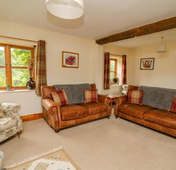 A living room with two brown leather sofas and a floral armchair at Byrdir Cottage in Rhayader