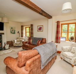 A living room with leather sofas floral armchairs a wood burning stove and windows with plaid curtains at Byrdir Cottage in Rhayader