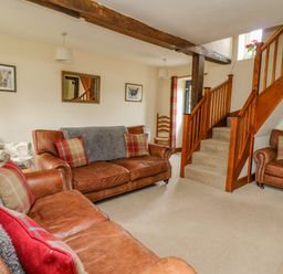 A living room with brown leather sofas and a wooden staircase at Byrdir Cottage in Rhayader