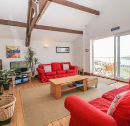 A living room with two red sofas a coffee table and sliding glass doors overlooking a balcony at Seascape in Trearddur Bay
