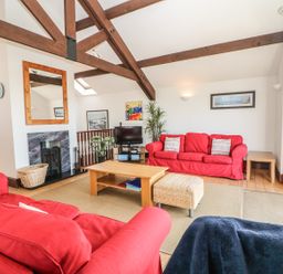 A living room with red sofas a wooden coffee table a fireplace and exposed wooden beams at Seascape in Trearddur Bay