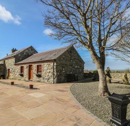 An outdoor area with a stone house and tree at Poppy Cottage in Caeathro near Caernarfon